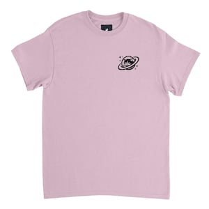 Könnte beinhalten: Hellrosa T-Shirt mit einer schwarzen Grafik einer Katze mit Sonnenbrille in einem Planetenring. Das Shirt hat einen Rundhalsausschnitt und kurze Ärmel. Die Katzen-Grafik befindet sich auf der oberen linken Brust.
