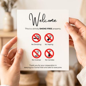 Könnte beinhalten: Eine weiße Karte mit dem Wort "Welcome" in eleganter Schrift. Darunter steht "This is a strictly SMOKE-FREE property." mit Symbolen, die Rauchen, Dampfen, Räucherstäbchen und Kerzen verbieten. Die Karte wirbt für eine rauchfreie Umgebung.