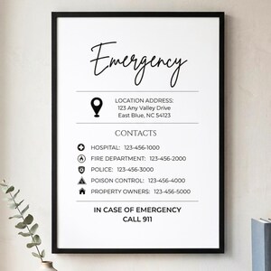 May include: A framed white print with the word "Emergency" in elegant script. Below, it lists a location address and emergency contact numbers for hospital, fire department, police, poison control, and property owners. The text "In case of emergency call 999" is at the bottom.
