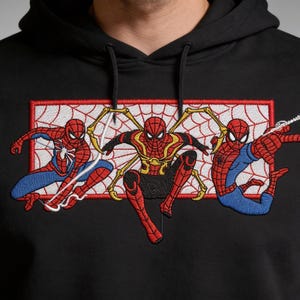 May include: Black hooded sweatshirt featuring an embroidered design of three Spider-Man characters in action poses. The design includes red, blue, and gold colors, set against a white and red web-like background.