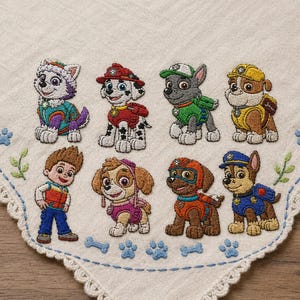 以下が含まれることがあります： カラフルな漫画の子犬と男の子の刺繍が施された白い生地。子犬たちは様々な衣装を着ており、生地はスカラップエッジ、足跡、骨のデザインで縁取られています。