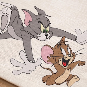 May include: Embroidered image of Tom and Jerry, the cartoon cat and mouse duo. Tom, in gray, is lunging with an angry expression. Jerry, in brown, is running with a joyful expression. The image is on a cream-colored fabric.