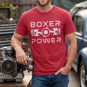 May include: A red short-sleeved t-shirt featuring the white distressed text BOXER POWER and a graphic of a flat engine piston assembly centered on the chest. The shirt is made of a cotton-like fabric and has a crew neckline and a standard fit.