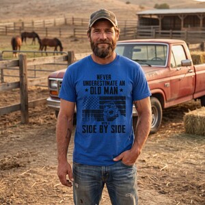 Könnte beinhalten: Ein leuchtend blaues Kurzarm-T-Shirt mit schwarzem Aufdruck auf der Brust, der den Text NEVER UNDERESTIMATE AN OLD MAN WITH A SIDE BY SIDE sowie eine Grafik einer amerikanischen Flagge und die Silhouette eines Fahrzeugs zeigt.