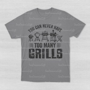 May include: A grey short-sleeved t-shirt featuring a black graphic print of various barbecue grills. The text reads YOU CAN NEVER HAVE TOO MANY GRILLS. The design includes illustrations of five different styles of outdoor cooking equipment.