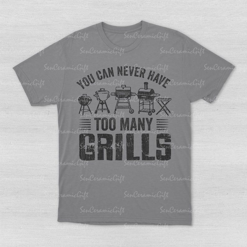 May include: A grey short-sleeved t-shirt featuring a black graphic print of various barbecue grills. The text reads YOU CAN NEVER HAVE TOO MANY GRILLS. The design includes illustrations of five different styles of outdoor cooking equipment.