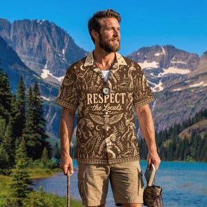 May include: A short-sleeved button-down shirt in brown with a cream-colored collar and a repeating pattern of mythical creatures and forest elements. The text "RESPECT the Locals" is printed in the center above a large eagle illustration.