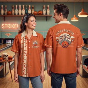 May include: A burnt orange short-sleeved bowling shirt with a cream-colored collar and button-down front. The shirt features a graphic on the back and front chest with the text Lucky Rollers, a pumpkin, and bowling pins. The front has a vertical pattern.