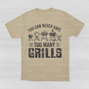 May include: A tan short-sleeve t-shirt featuring a black graphic print of various barbecue grills and the text "YOU CAN NEVER HAVE TOO MANY GRILLS" in a distressed, bold font. The design is centered on the chest of the crew neck garment.