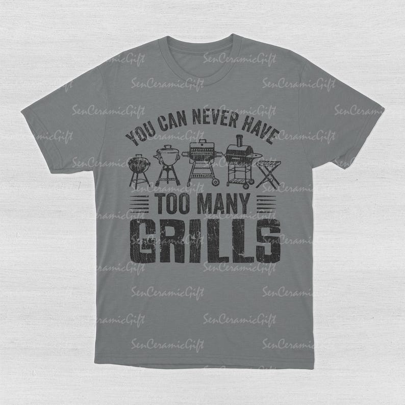 May include: A grey short-sleeved t-shirt featuring a black graphic print of various barbecue grills and the text "YOU CAN NEVER HAVE TOO MANY GRILLS" in a distressed font. The design is centered on the chest of the shirt.