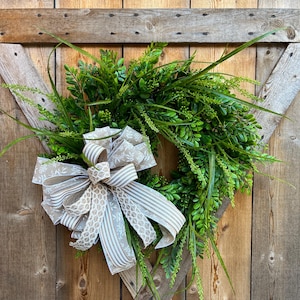 May include: A green leafy wreath with a brown and white patterned bow, hanging on a wooden door.