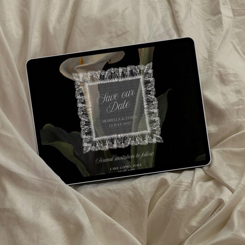Puede incluir: Una tableta digital muestra un dise&ntilde;o de invitaci&oacute;n de boda. La invitaci&oacute;n presenta el texto "Save our Date" en una escritura elegante, enmarcado por un delicado borde de encaje. El fondo es un dise&ntilde;o floral negro con calas blancas. La fecha es el 22 de julio de 2027.