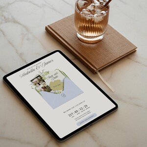 May include: A digital tablet displays a wedding invitation with the names "Arabella & James" and "Save our Date". A brown notebook and a glass of iced beverage sit beside the tablet. The invitation includes a date and time.