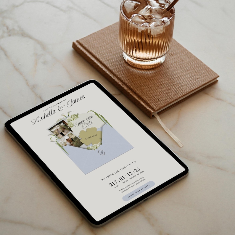 May include: A digital tablet displays a wedding invitation with the names "Arabella & James" and "Save our Date". A brown notebook and a glass of iced beverage sit beside the tablet. The invitation includes a date and time.