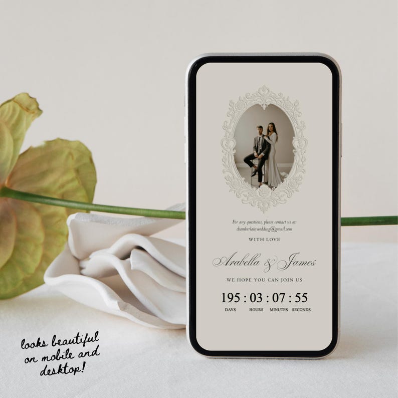 K&ouml;nnte beinhalten: Ein Smartphone zeigt eine digitale Hochzeitseinladung mit beigem Hintergrund, einem verzierten ovalen Rahmen mit einem Foto eines Paares und dem Text Arabella & James. Darunter zeigt ein Countdown 195 Tage, 03 Stunden, 07 Minuten und 55 Sekunden an.