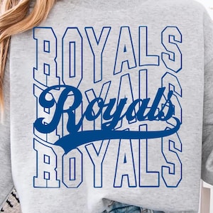 May include: A light gray sweatshirt with the word "ROYALS" in blue, stacked vertically and horizontally. The word "Royals" is also written in a cursive font in the center. A person is holding a green mug.