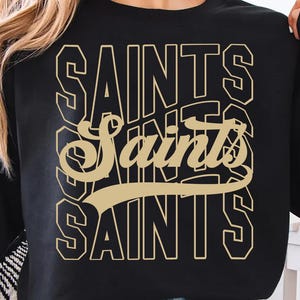 以下が含まれることがあります： 黒色の長袖スウェットシャツ。金色の文字で「SAINTS」と書かれています。この単語は3回重ねてあり、真ん中の単語は筆記体です。カジュアルなスタイルの衣服です。