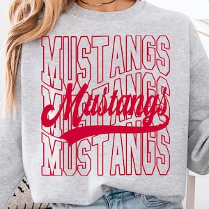 May include: A light gray sweatshirt with the word "MUSTANGS" in red block letters stacked vertically. A cursive "Mustangs" is centered in red. The person is holding a green mug that says "COFFEE".
