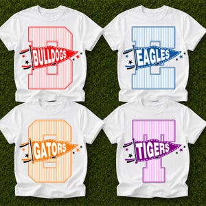 Könnte beinhalten: Vier weiße Kurzarm-T-Shirts mit großen, vertikal gestreiften Buchstaben B, E, G und T. Jeder Buchstabe ist mit einer Wimpelgrafik überlagert, die den Text BULLDOGS, EAGLES, GATORS oder TIGERS in Rot, Blau, Orange und Lila enthält.