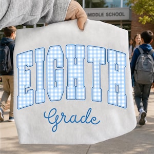 May include: A white t-shirt featuring the word EIGHTH in large, block-style letters with a light blue and white gingham pattern, followed by the word Grade in a blue cursive script font centered below the block text.