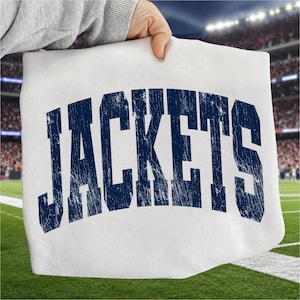 May include: A white t-shirt featuring the word JACKETS printed in a large, arched, dark navy blue font with a distressed, weathered texture. The lettering is bold and capitalized, centered on the front of the garment fabric.