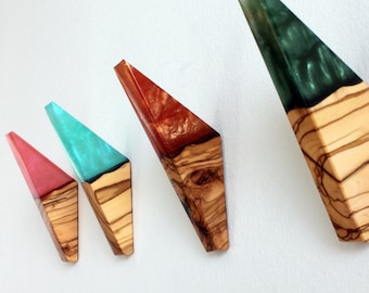 May include: Four decorative wooden objects with colorful resin tops. The objects are triangular, with a natural wood base and resin in shades of pink, turquoise, red, and green. The wood grain is visible.