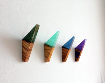 May include: Four wall hooks with a geometric design. The hooks are made of wood and resin, with colors including green, teal, blue, and purple. The wooden base has a natural wood grain pattern.