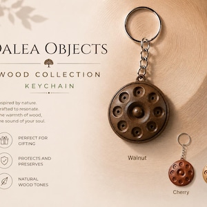 Könnte beinhalten: Drei kreisförmige Holzschlüsselanhänger mit einer zentralen Erhebung und acht umlaufenden Vertiefungen, befestigt an silbernen Metallringen. Die Anhänger sind als Walnut, Cherry und Oak beschriftet und zeigen verschiedene Brauntöne.