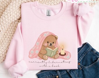 Sudadera unisex con cuello redondo "Oso Acogedor Hibernando con un Libro"
