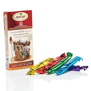 May include: A box of Manisa Mesir Macunu, a Turkish spice paste, with colourful wrapped sweets. The box is red and white with text in multiple languages. The sweets are in yellow, red, green, blue, and purple wrappers.