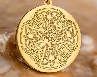 May include: Gold-colored pendant necklace featuring a circular pendant with an intricate Celtic cross design. The pendant is suspended from a delicate gold chain. The background is a blurred, neutral tone, highlighting the jewelry.
