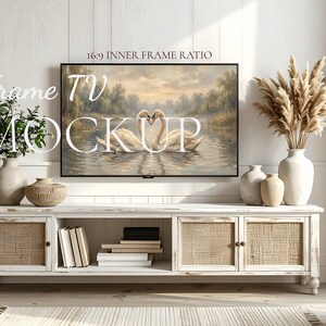 May include: A white distressed TV stand with woven cabinet doors and a painting of swans on a lake. The TV is mounted on a white wall. Decorative vases and books are on the stand. The text "Frame TV Mockup" is on the image.