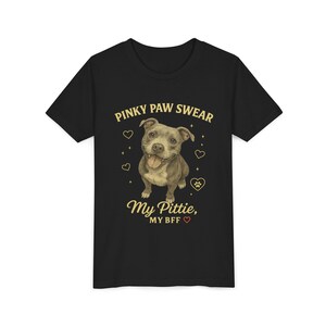 Puede incluir: Camiseta negra con una ilustración de un pitbull sonriente y el texto "Pinky Paw Swear, My Pittie, My BFF" en dorado. El diseño incluye corazones y una huella de pata.