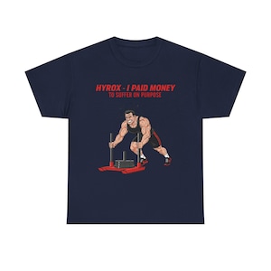 Puede incluir: Camiseta azul marino con el texto "HYROX - I PAID MONEY TO SUFFER ON PURPOSE" en rojo. La camiseta presenta un gráfico de una persona musculosa empujando un trineo con peso. La persona lleva pantalones cortos negros y zapatos rojos.