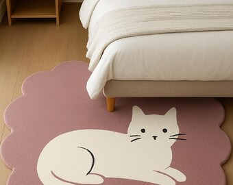 May include: A decorative rug featuring a white cat design on a mauve background. The rug has a scalloped edge and is placed on a hardwood floor near a bed. The cat illustration has black whiskers and a curved tail.