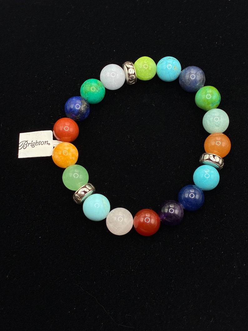 May include: A stretch bracelet featuring multicolored round beads in shades of blue, green, orange, red, purple, and white, interspersed with silver-toned metal spacers. A white rectangular tag with the word Brighton is attached to the bracelet.