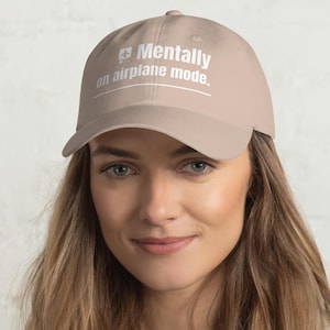 Puede incluir: Gorra de béisbol beige con el texto blanco "Mentally on airplane mode". La gorra tiene una visera curva y un diseño sencillo, adecuado para uso informal. El sombrero está hecho de un material suave.