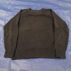 May include: A dark gray sweater with a ribbed hem and cuffs. The crew neck has a white and gray striped detail. The sweater is made of a soft, knitted material and is suitable for casual wear.