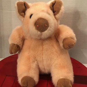 May include: A plush pig toy in shades of peach and brown. The pig has large ears, a round snout, and small, dark eyes. The toy is soft and cuddly, perfect for children.
