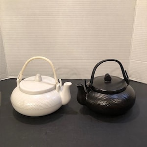 以下が含まれることがあります： くぼみのある質感の白いティーポットと明るい色の湾曲したハンドル、そして同じくくぼみのある質感の黒いティーポットと黒い湾曲したハンドル。両方のティーポットには、丸い本体、蓋、注ぎ口が付いています。