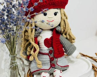 May include: A handmade crochet doll with blonde hair, wearing a red beret and jacket over a white shirt with a red heart. The doll has a gray skirt and red shoes. The doll is sitting on a white tray with lavender and a glass vase.