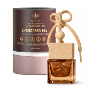 Puede incluir: Una botella de vidrio color ámbar con tapa de madera y cordón beige, junto a un recipiente cilíndrico. La botella está etiquetada como "EVERGREEN MIST" y "AMBER COLLECTION". El recipiente es marrón y rosa, con texto que indica aceites esenciales.