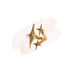 May include: A gold-colored ring with a unique design featuring three starburst shapes. The ring has a modern, geometric aesthetic, with a polished finish. The ring is set against a white background with a subtle, abstract brushstroke.
