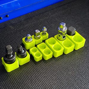 May include: A collection of bright lime green plastic socket organizers arranged in a row. Several metal socket adapters and universal joints are inserted into the holders, while some of the square-shaped slots remain empty for additional tools.
