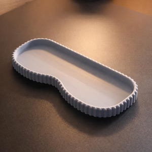 May include: A light blue, oblong tray with a scalloped edge. The tray has a smooth interior and a curved design on one end. The tray is made of a solid material and sits on a dark surface.