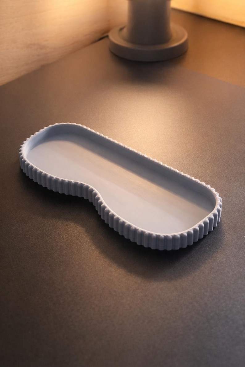 May include: A light blue, oblong tray with a scalloped edge. The tray has a smooth interior and a curved design on one end. The tray is made of a solid material and sits on a dark surface.
