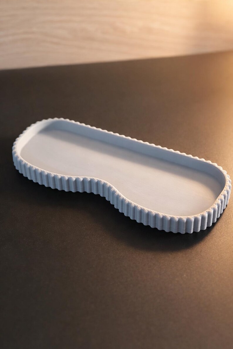 May include: A light blue, oblong decorative tray with a scalloped edge. The tray has a smooth interior and a wavy, asymmetrical design. The tray is made of a solid material and is suitable for displaying small items.