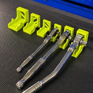 Peut inclure: Ensemble de clés à cliquet chromées avec des supports vert fluo. Les outils sont disposés sur une surface noire, avec un fond bleu. Les supports sont étiquetés avec des mesures de taille.