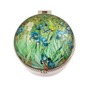 May include: Round, silver-toned compact mirror featuring a colorful floral design reminiscent of a painting. The artwork showcases blue irises, green foliage, and yellow accents. The compact has a hinged opening and a decorative beaded edge.