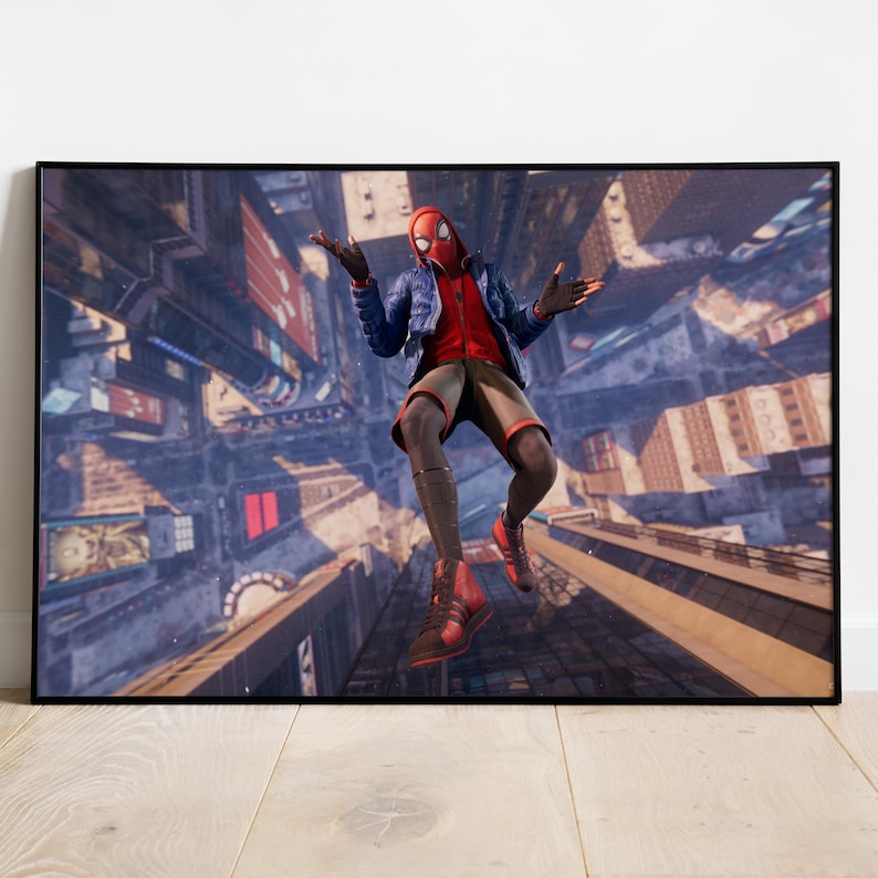 May include: A framed print featuring a character in a red and black suit with a mask, mid-air above a cityscape. The character wears a blue jacket and shorts. The background shows a detailed aerial view of buildings and streets.